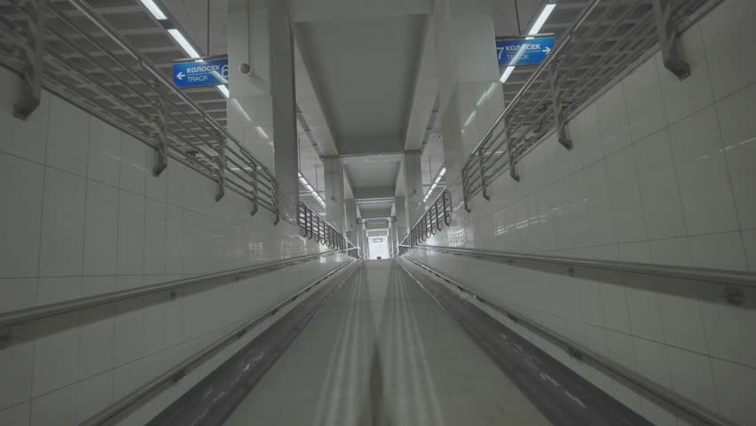 Subterranean corridor passage with bright lights and metal railings.