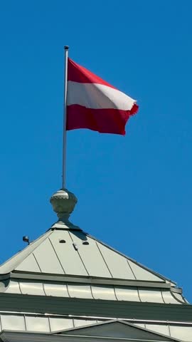 Austrian National Flag Waving on Rooftop Against Clear Blue Sky