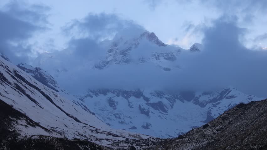 Timelapse landscape along the Annapurna Base Camp Trek in Nepal featuring snow-covered Himalayan peaks, drifting clouds, and dramatic mountain scenery. Towering mountains rise above deep valleys and rugged terrain, while changing weather conditions create constant movement across the sky. Clouds flow around the high peaks, revealing and concealing sections of the mountain range throughout the sequence. The video captures the scale and beauty of the Annapurna region, one of the most famous trekking destinations in the Himalayas. Natural light, alpine landscapes, and dynamic cloud formations combine to create a striking view of the high-altitude wilderness of Nepal