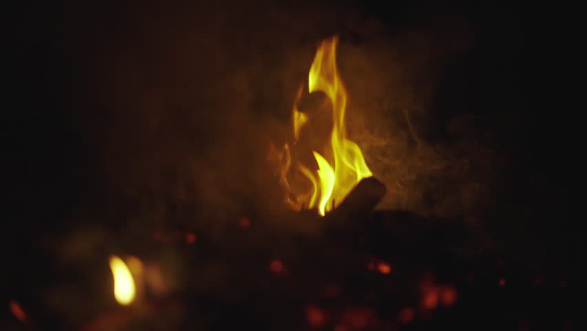 Nighttime fire, glowing embers, crackling flames, smoke.