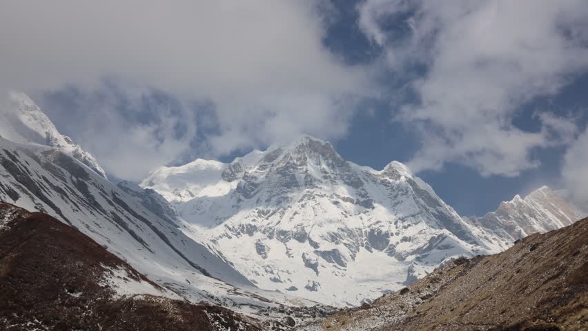 Timelapse landscape along the Annapurna Base Camp Trek in Nepal featuring snow-covered Himalayan peaks, drifting clouds, and dramatic mountain scenery. Towering mountains rise above deep valleys and rugged terrain, while changing weather conditions create constant movement across the sky. Clouds flow around the high peaks, revealing and concealing sections of the mountain range throughout the sequence. The video captures the scale and beauty of the Annapurna region, one of the most famous trekking destinations in the Himalayas. Natural light, alpine landscapes, and dynamic cloud formations combine to create a striking view of the high-altitude wilderness of Nepal