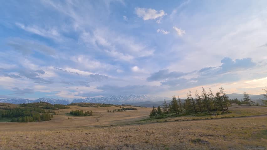 Time lapse of clouds moving over a vast alpine meadow with snow-capped Altai Mountains in the background