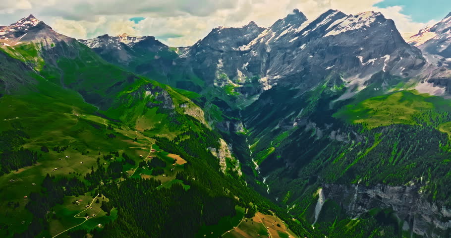 Establishing shot of Switzerland. Aerial view of the green meadows of Switzerland, with the Alps and clouds in the background