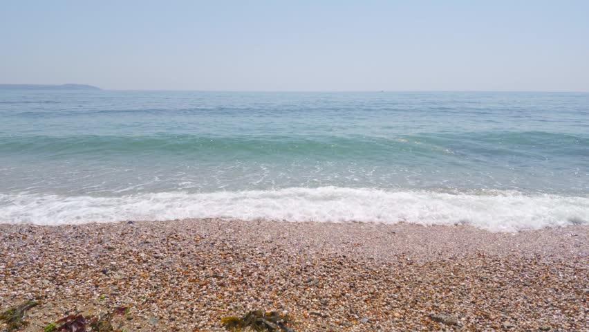 Water waves breaking onto a coarse shingle shoreline with clear turquoise sea and light blue sky. Charlestown United Kingdom