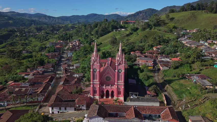 Aerial view approaches pink Gothic church in Jerico, surrounded by green hills and town