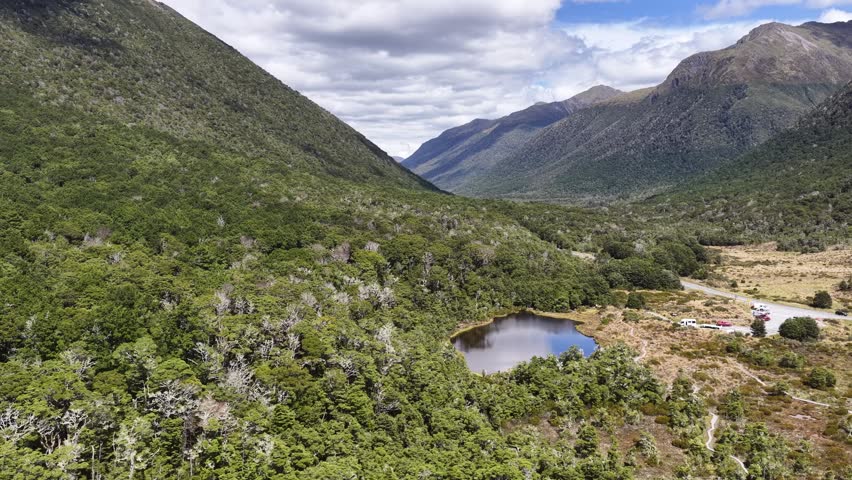 Aerial view of a dramatic mountain valley with a river winding through lush green hills under cloudy skies in New Zealand South Island.