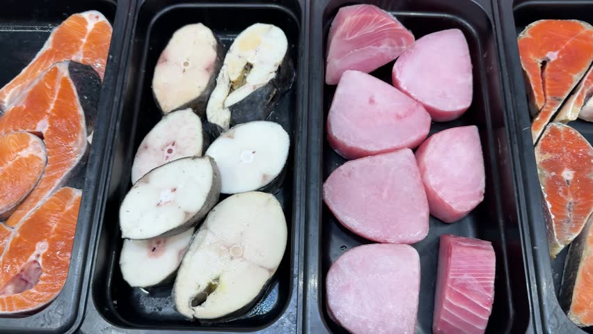 Frozen tuna trout salmon steaks displayed on black trays with ice crystals, close-up of pink tuna portions, white trout medallions
