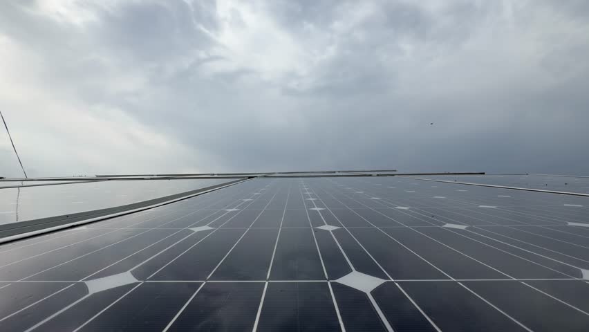 Solar panels installed in a graveyard overlook a lush landscape, rainfall cascading under heavy, dark clouds.