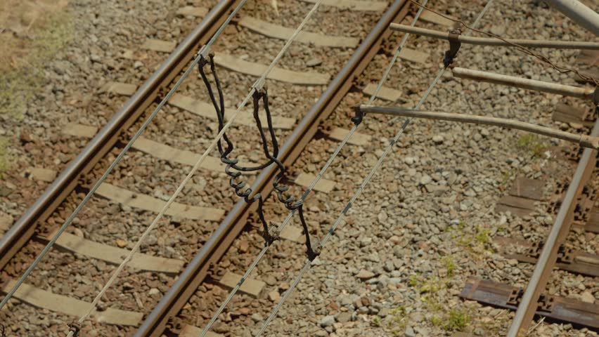 Electric wires and current dividers set up over the railway tracks. The setup connects power for trains along the rails during a sunny day.