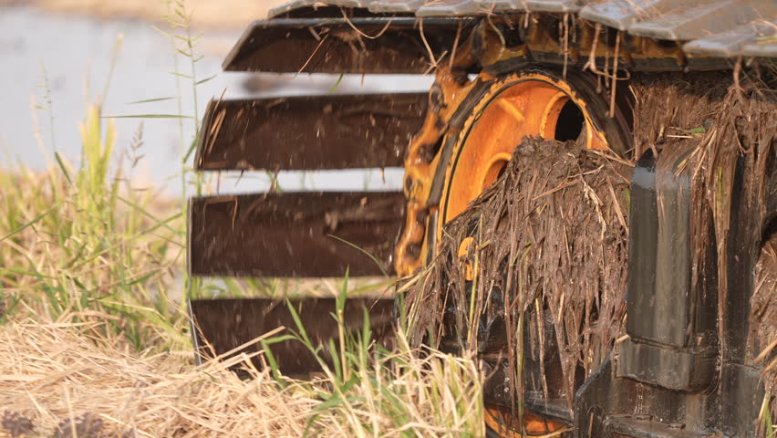 Water wheel mill by river with rustic wooden machinery, grass, nature countryside, vegetation, muddy tractor tire, excavator tread, wet field soil near stream pond
