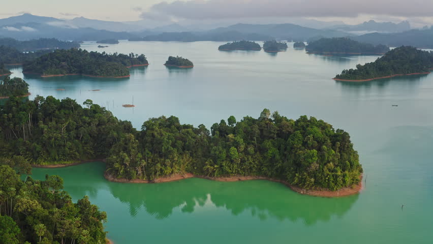 Breathtaking aerial view of Cheow Lan Lake turquoise waters and lush rainforest islands framed by dramatic limestone karsts in Khao Sok National Park, Thailand. Nature landscape. Drone flight panorama