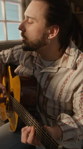 Young adult Caucasian man playing acoustic guitar and singing in home studio. Clip is suitable for music education platforms, creative hobby advertisements, or lifestyle marketing, vertical