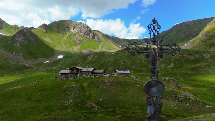 The mountain cross in front of the Mont Fallère mountain hut in the Aosta Valley, Italy, with the refuge full of tourists in the background