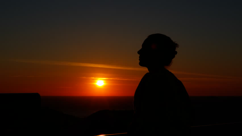 Woman silhouette enjoying a beautiful mountain sunset. Woman in silhouette with her hair in a bun looking at a beautiful sunset from a viewpoint, contemplating the stunning view of the sun setting