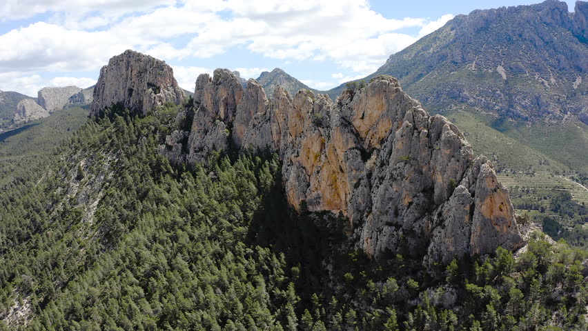 Aerial view of Els Castellets in Alicante, Spain. Dramatic rocky ridge with steep cliffs and dense Mediterranean pine forest on western slopes within rugged mountainous landscape. 