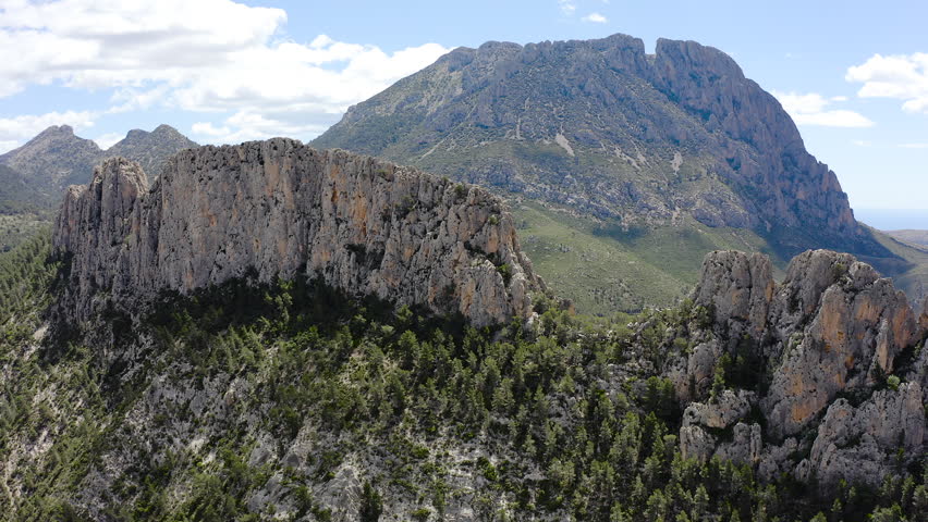 Aerial view of Els Castellets in Alicante, Spain. Dramatic rocky ridge with steep cliffs and dense Mediterranean pine forest on western slopes within rugged mountainous landscape. 