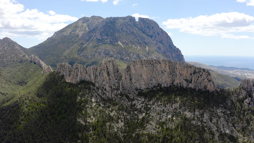 Aerial view of Els Castellets in Alicante, Spain. Dramatic rocky ridge with steep cliffs and dense Mediterranean pine forest on western slopes within rugged mountainous landscape. 