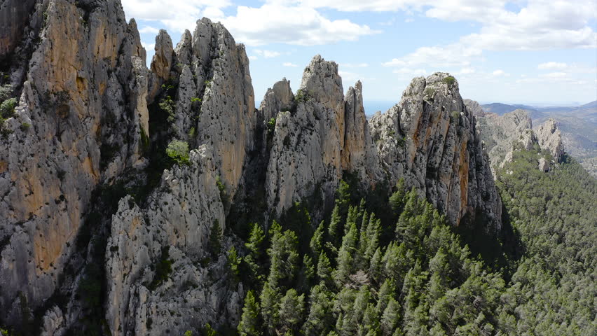 Aerial view of Els Castellets in Alicante, Spain. Dramatic rocky ridge with steep cliffs and dense Mediterranean pine forest on western slopes within rugged mountainous landscape. 