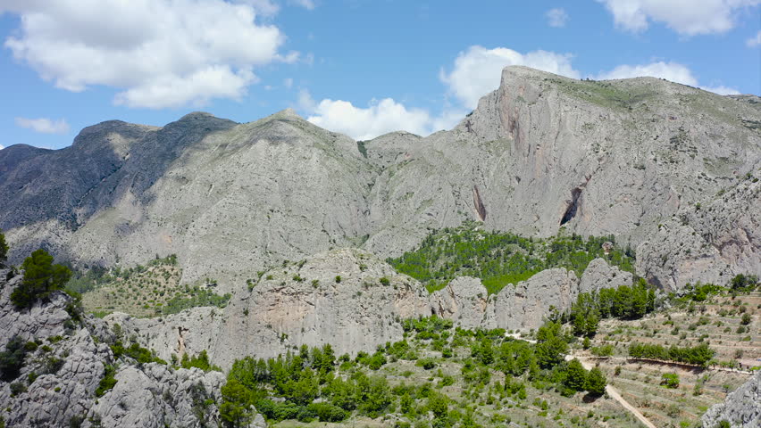Aerial view of Els Castellets in Alicante, Spain. Dramatic rocky ridge with steep cliffs and dense Mediterranean pine forest on western slopes within rugged mountainous landscape. 