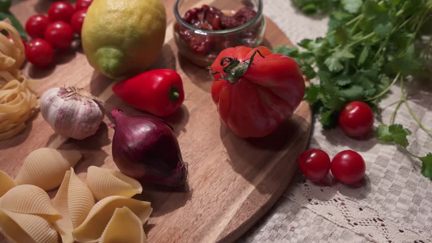 Close-up of fresh tomatoes, garlic, onions, lemon, and pasta arranged on a wooden board in a kitchen setting