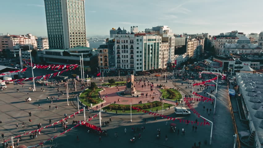 Aerial cinematic view of Taksim Square and the Republic Monument with walking people and traffic in Istanbul, Turkey.