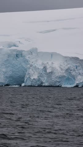 Towering ice cliff of a glacier front under a grey sky beside dark Antarctic waters.