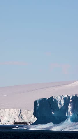 Sunlit ice cliff of a glacier front rising above the dark Southern Ocean in Antarctica.