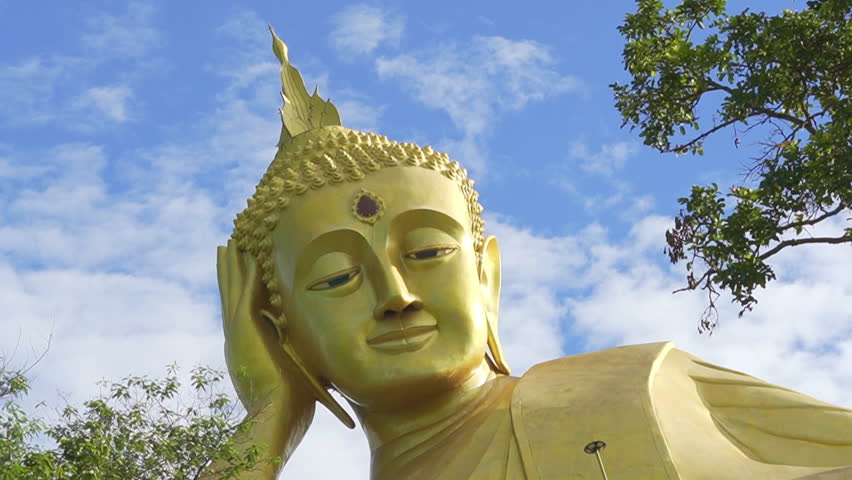 Large golden reclining Buddha statue with moving clouds in the blue sky, Thailand.