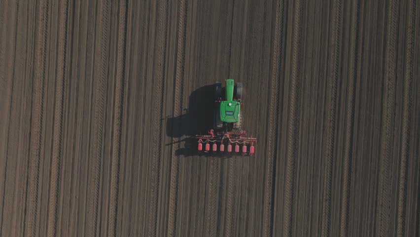 Aerial view of tractor planting corn on brown field landscape.