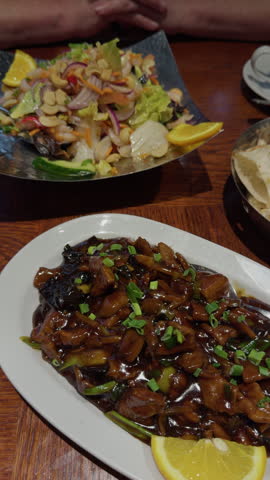 Glazed noodle dishes with vegetables, lemon garnish, and fresh salad on wooden table