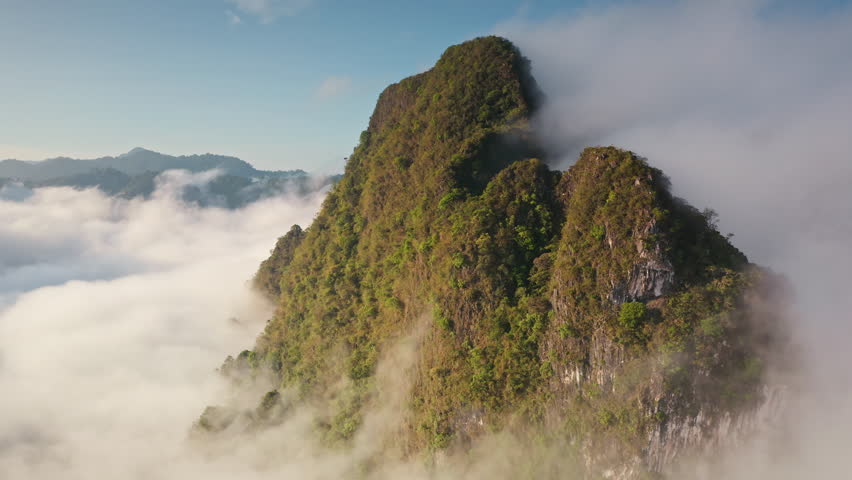 Limestone mountains with tropical jungle vegetation rising above thick blanket of morning fog, breathtaking aerial view of natural landscape in Khao Sok National Park, Thailand. Drone flight panorama