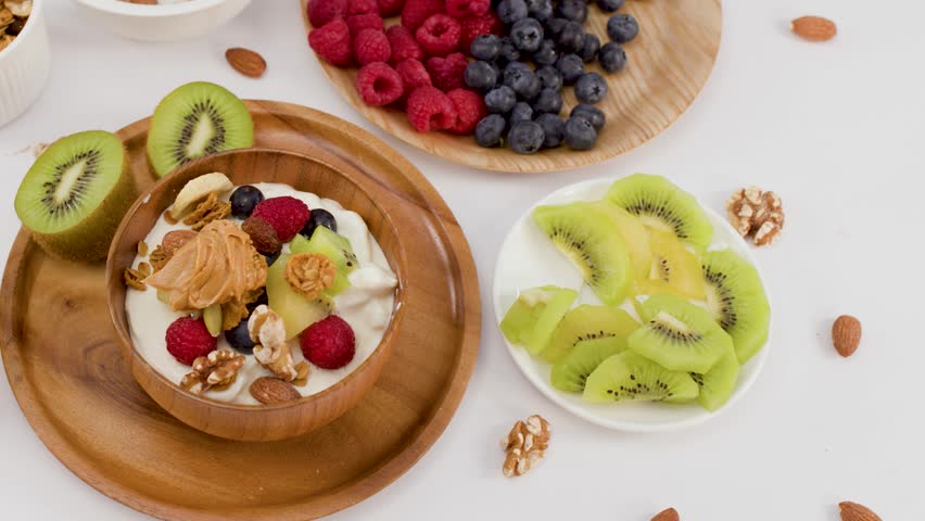 Overhead shot of hands lifting a wooden bowl filled with yogurt, berries, and nuts.