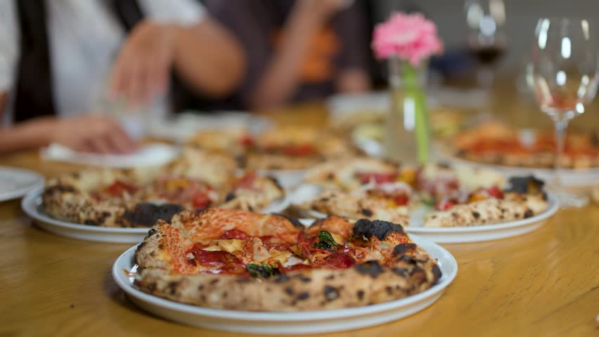 Close-up of hands taking slices of fresh pizza from wooden tables in a restaurant.
