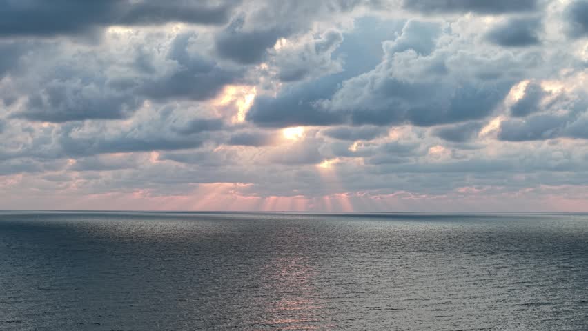 Dark clouds fill the sky. Sunlight pierces cloud layers. Golden beams shine on the ocean