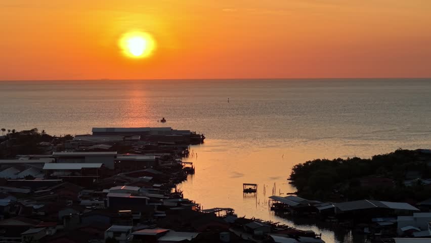 Golden sunset reflecting over coastal fishing village and calm sea at Tanjung Piandang.