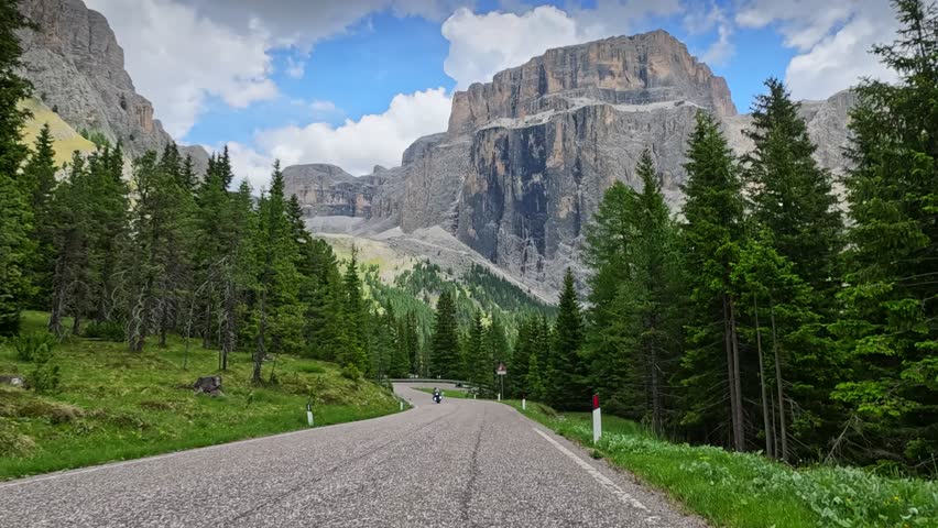 Riding motorbike on scenic pass road with stunning mountain view, driving on asphalt serpentine highway in Dolomites towards giant rocky cliff. Motorcycle trip in South Tyrol region, Italy