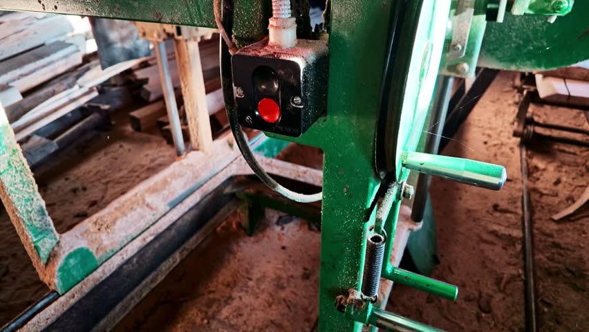 Carpenter pressing red button on woodworking machine to start sawing timber log in a sawmill