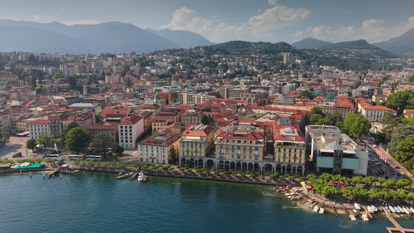 Aerial shot of Lugano city waterfront and calm lake, scenic view of luxury Swiss resort surrounded by green mountains. Blue waters of Lugano lake looking at beautiful alpine city