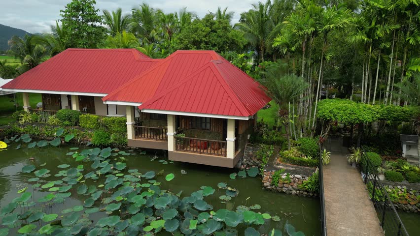A rising tilt-down aerial reveals red-roofed villas over lily-filled ponds and tropical trees Palaisdaan Hotel, Bagabag, Nueva Vizcaya, Philippines
