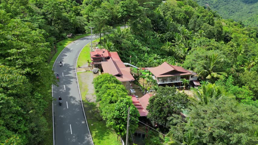 Side view aerial of resort hotel with red-roofed buildings, winding road, tropical trees, and mountain backdrop in Tanay Rizal, Philippines.