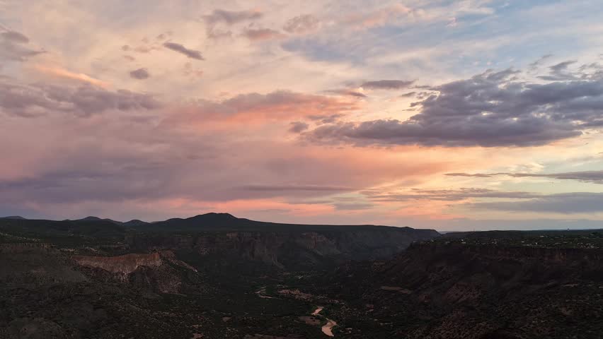 A sweeping drone timelapse of a vast Southwest canyon under a pastel sunset. Expansive clouds drift dynamically across the sky as the Rio Grande winds through the rugged valley below.