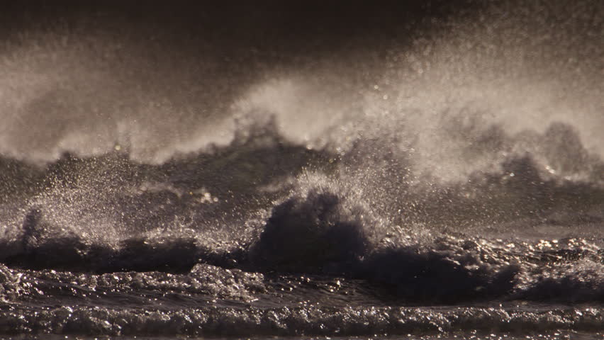 Turbulent ocean waves crash onto beach on windy day at sunset, telephoto slomo