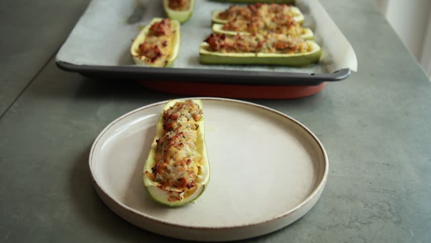 Close-up of baked zucchini boats stuffed with savory pork mince, topped with melted cheddar cheese and freshly chopped parsley, served on a white plate