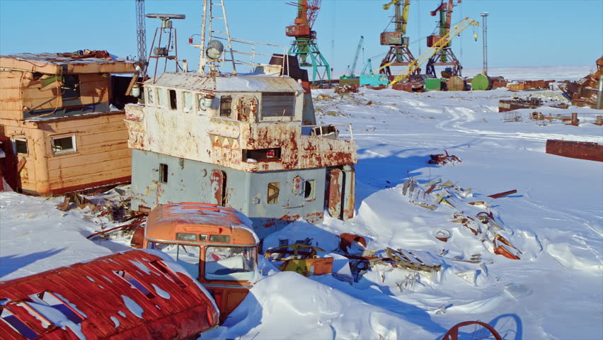 Rusty abandoned ships and scrap metal at a frozen port in the Arctic region during winter