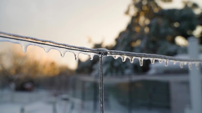 Ice covered metal fence wire with icicles at sunrise close-up