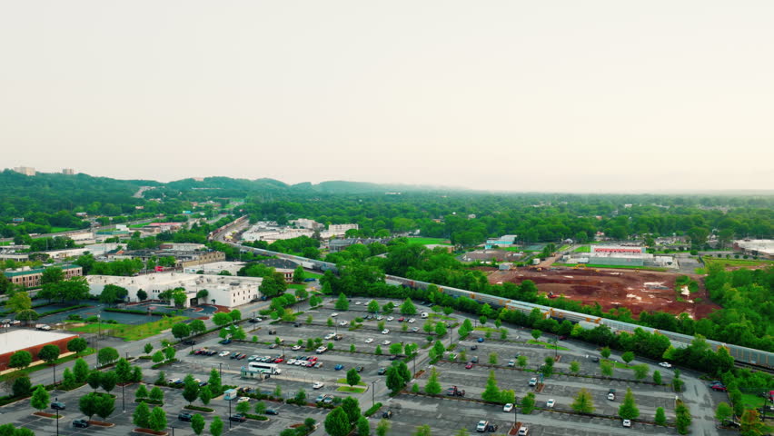 Long freight train transporting cargo through a developed suburban area of Birmingham, Alabama, with parking facilities and greenery.