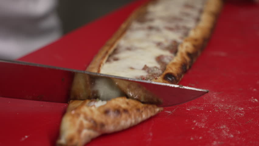 Professional chef in a restaurant kitchen slicing a traditional Turkish pide on a red cutting board, fa01