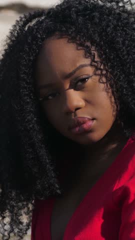 A young African American woman shows her serious and somewhat sad face on camera, while her hair, standing in the street, sways in the wind. 