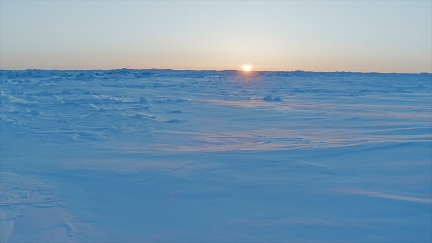 Golden sun setting over a vast, frozen, and snowy arctic landscape during a cold winter day