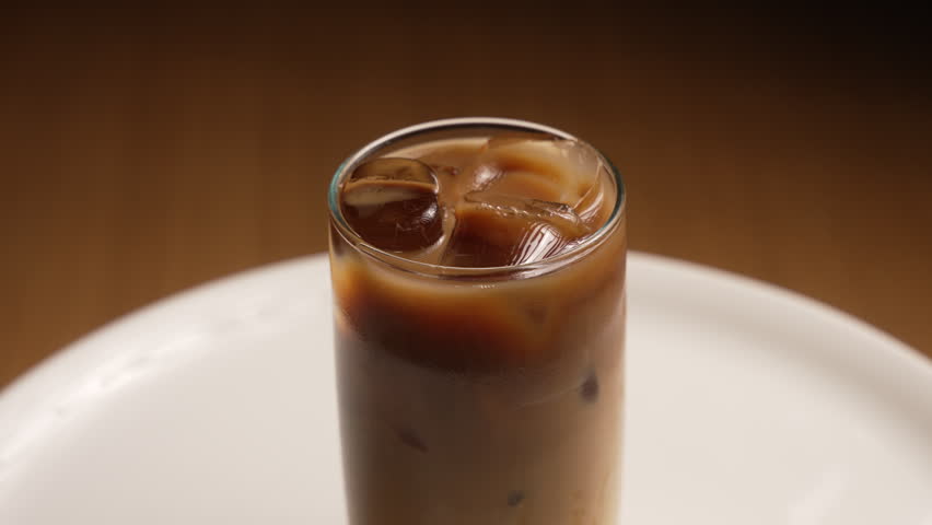 Iced coffee rotating on a white plate against a wooden background, fa01